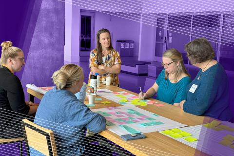 Group of five women at a table with large papers covered in colorful post-its