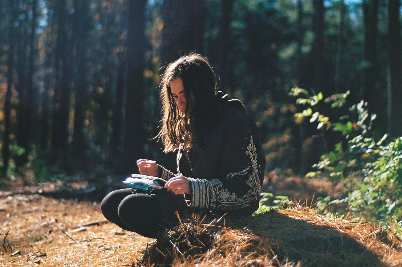 Photograph of a teen seated at the edge of a treed area.