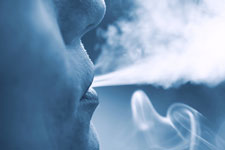 Photograph of a person's face breathing out vapor.