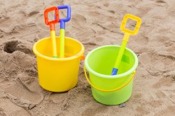 Photograph of two plastic buckets with plastic shovels side by side on a sandy beach.