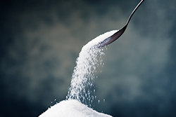 Photograph of a spoon pouring sugar onto a pile.