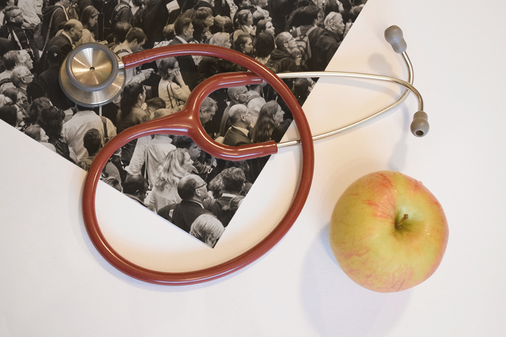 Photograph of a stethoscope and apple resting on a photo of a crowd of people.