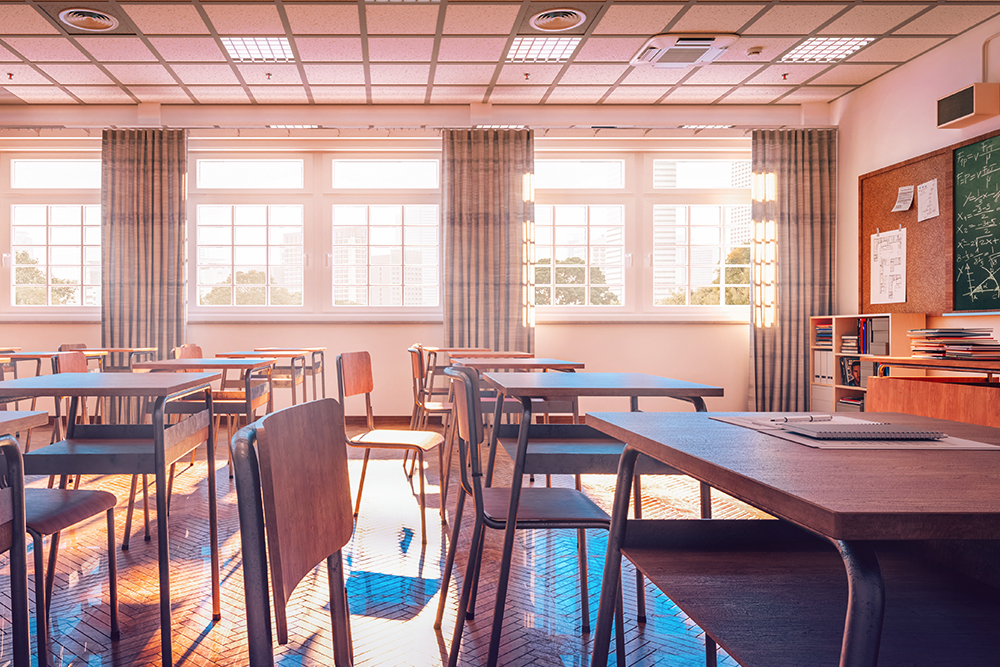 Photograph of a classroom with big, bright windows, desks and chairs.