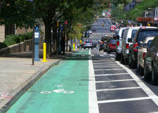 Photograph of a bicycle lane between a sidewalk and car traffic lanes.