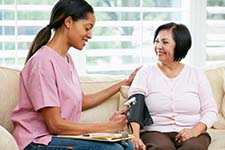 Photograph of a health care provider checking a client's blood pressure in a home setting.