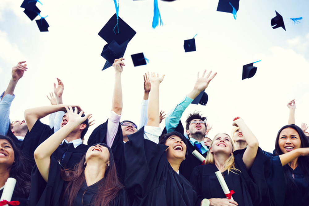 Photograph of graduates in regalia tossing their mortarboard hats.